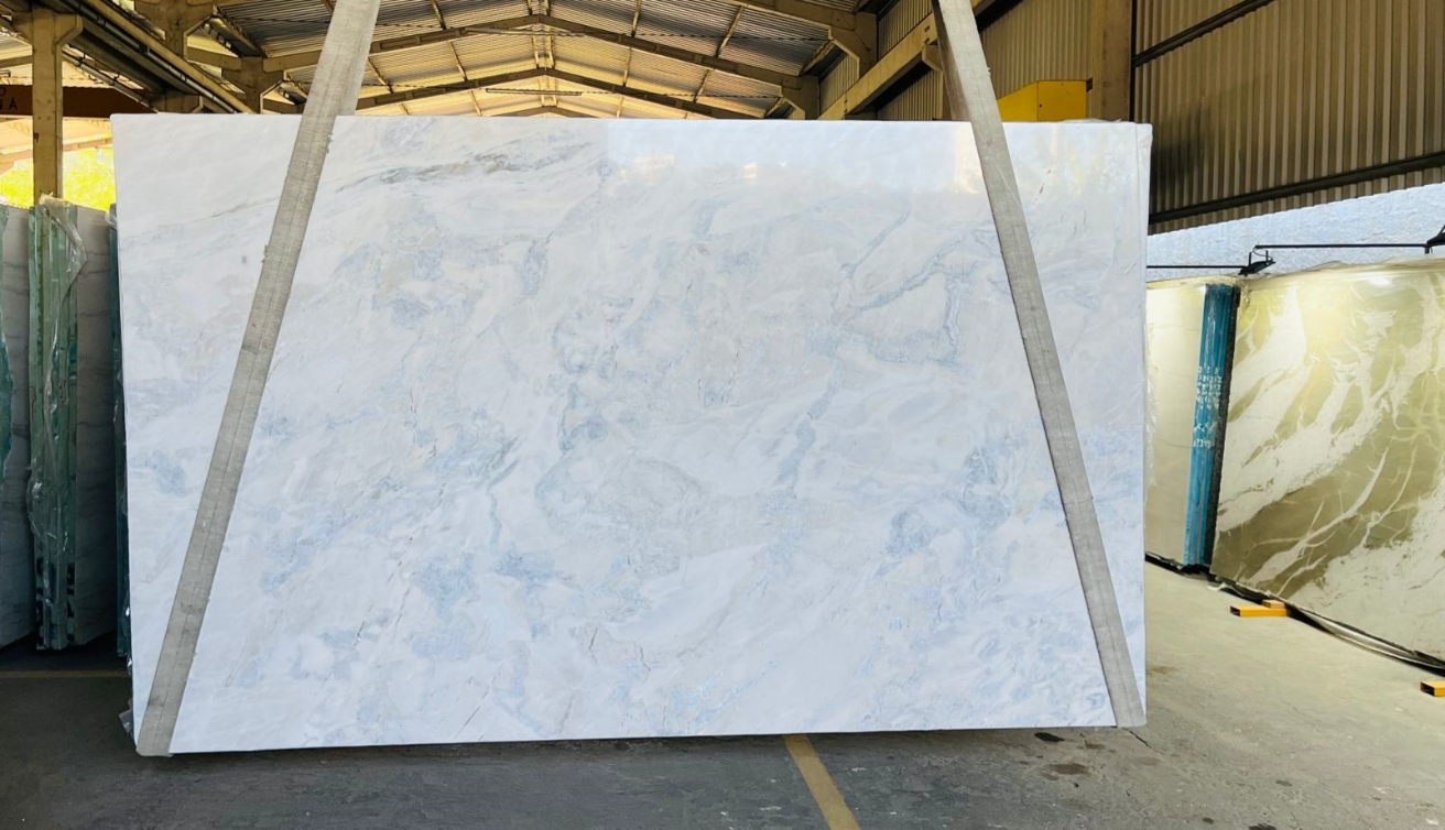 A large white marble slab is being lifted by a crane in a warehouse.