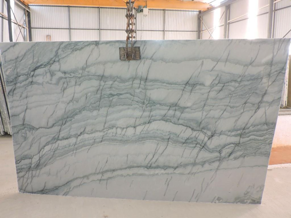 A large white marble slab is sitting in a warehouse under a crane.