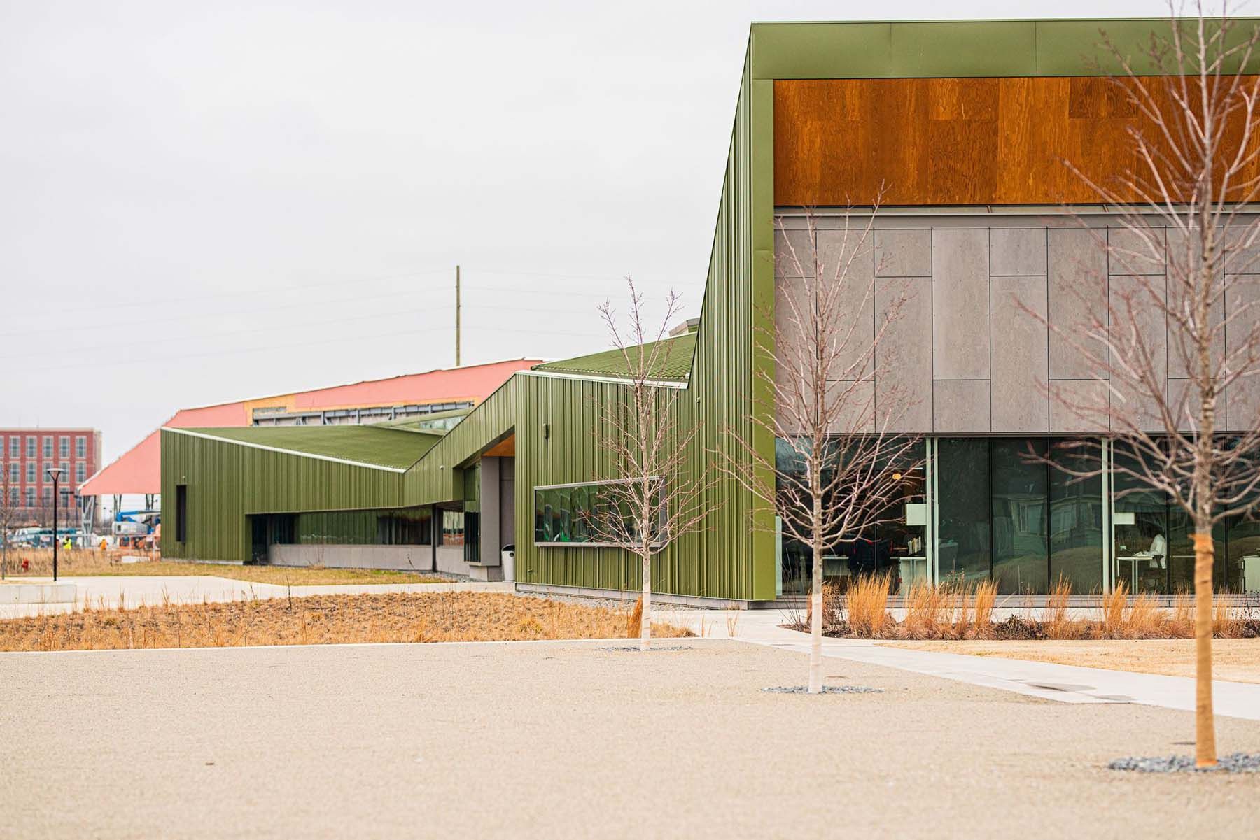 A large green building with a red roof and trees in front of it.
