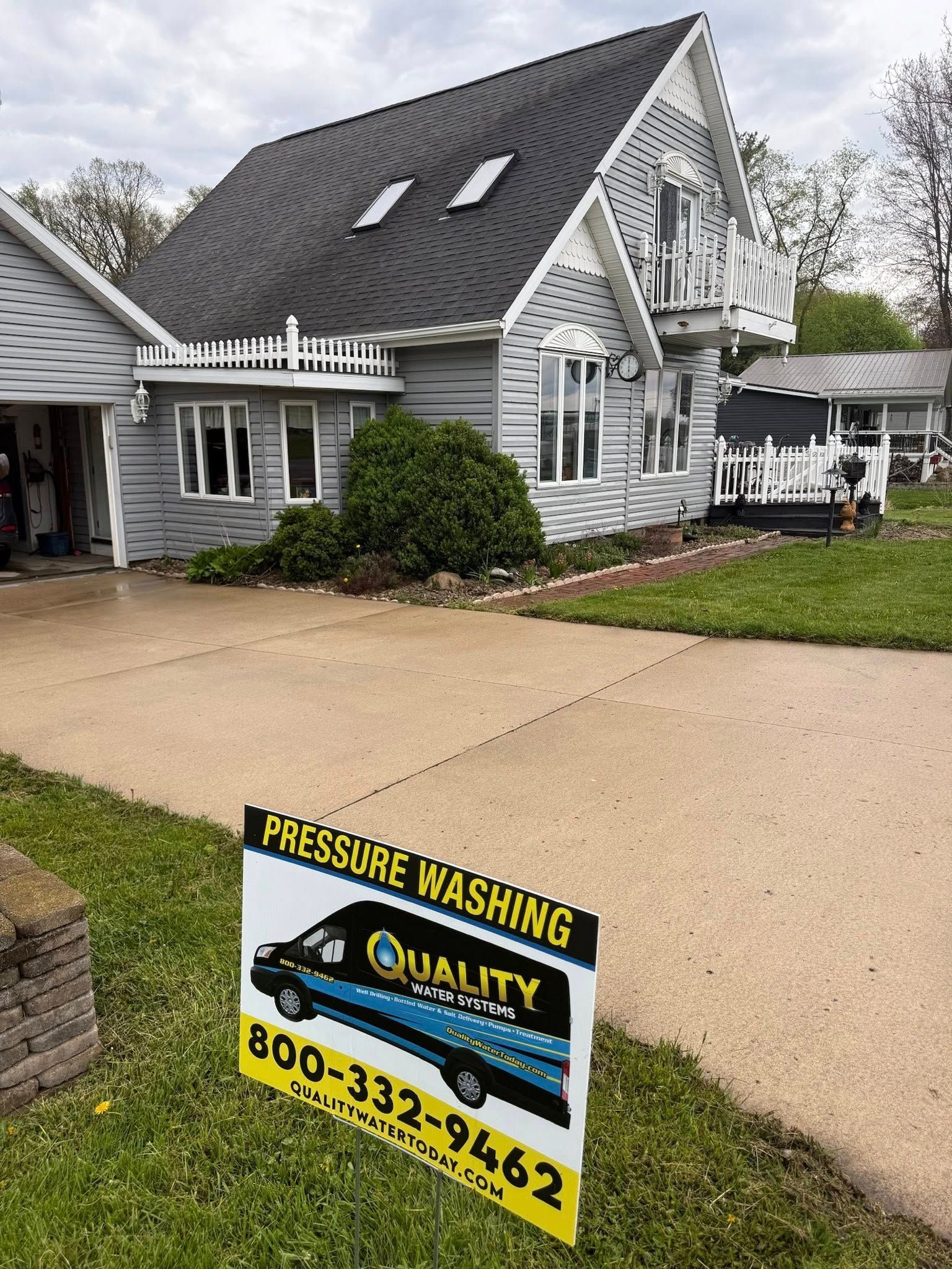 A gray house and driveway in front of a pressure washing business sign on a lawn.