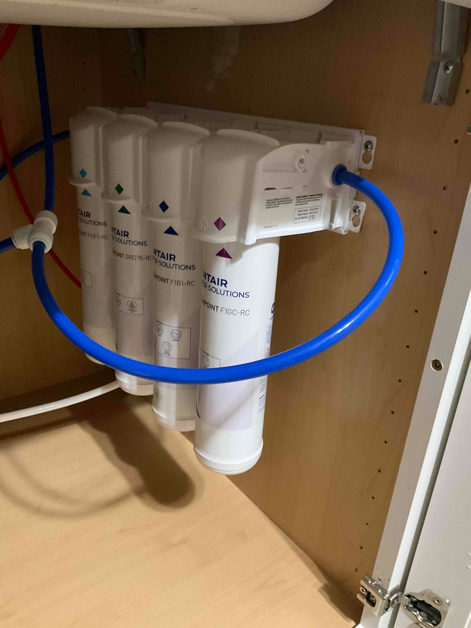 A four-stage under-sink water filtration system with white cylindrical cartridges mounted inside a cabinet.