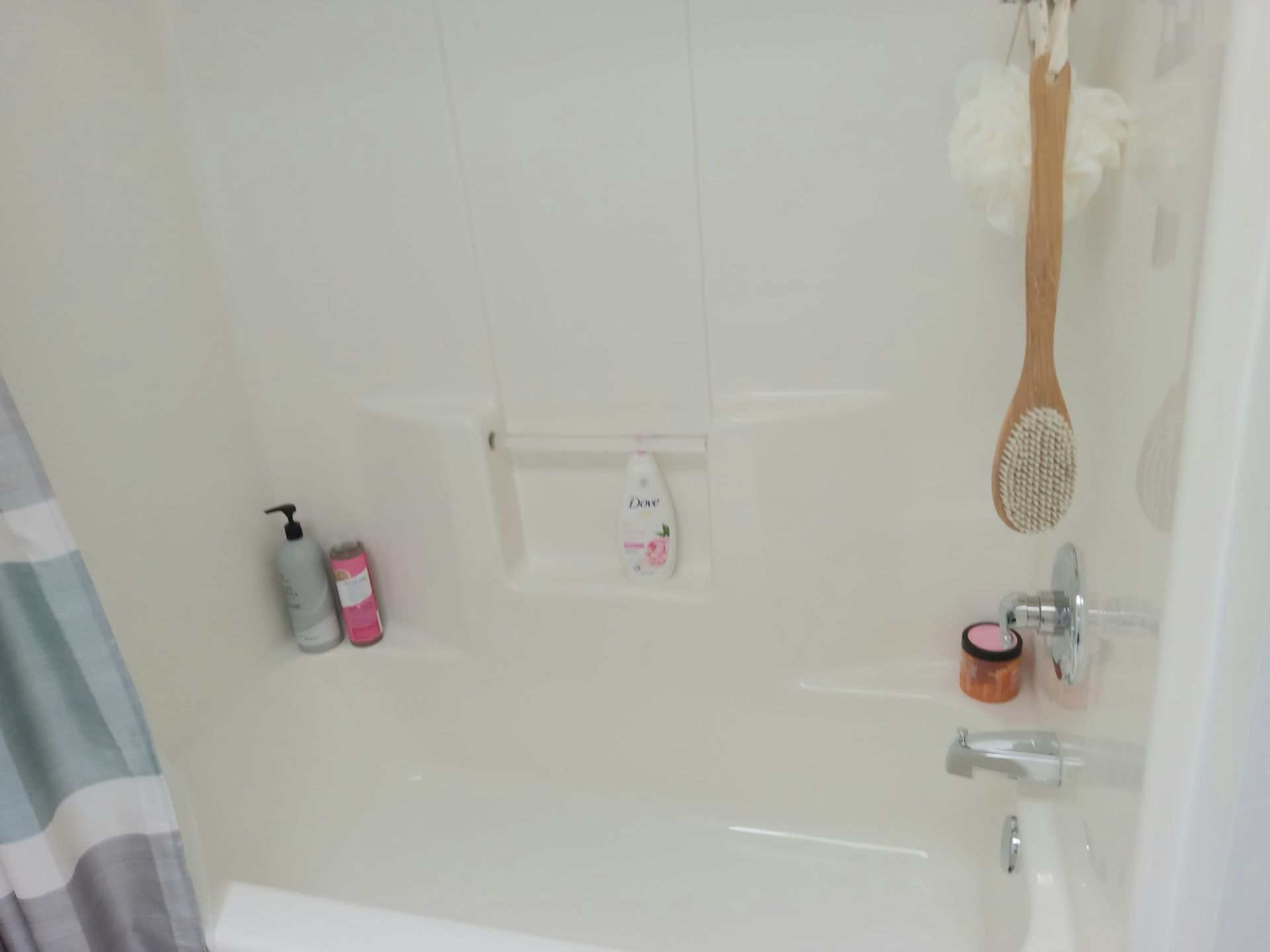 A white acrylic shower and bathtub unit with bottles and a scrubbing brush on the ledges.