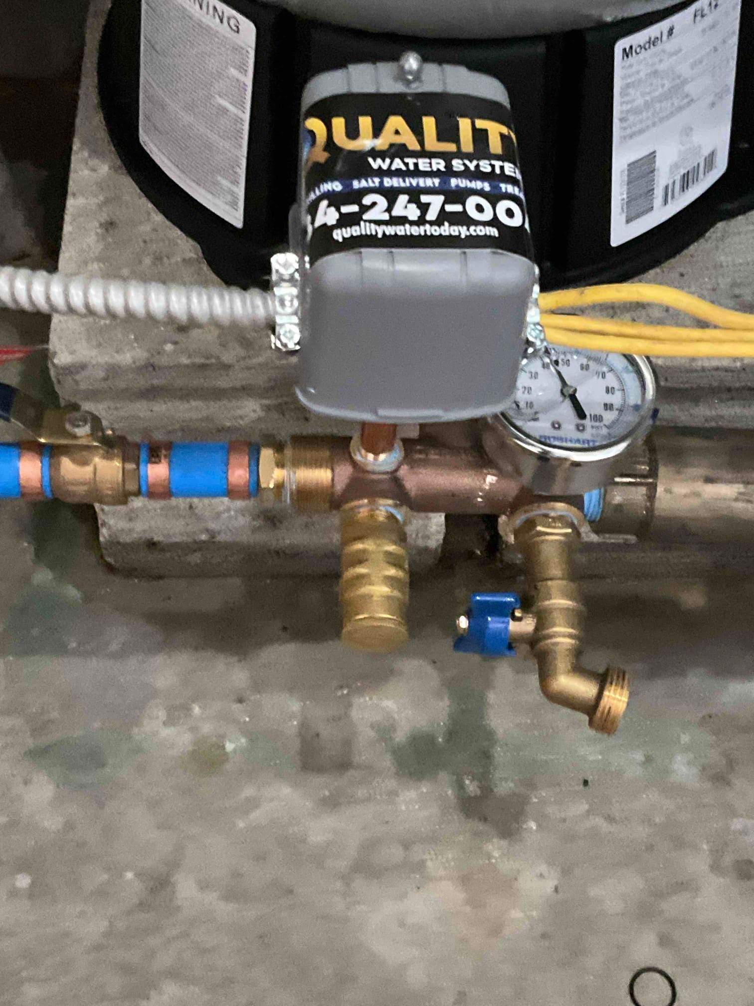 A water system control unit with a pressure gauge and valve fittings mounted on a pipe assembly.
