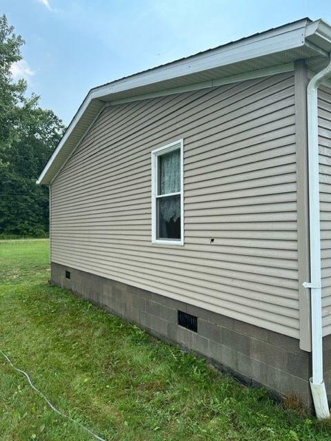 Side view of a house with beige horizontal vinyl siding, a single window, and a concrete block foundation.