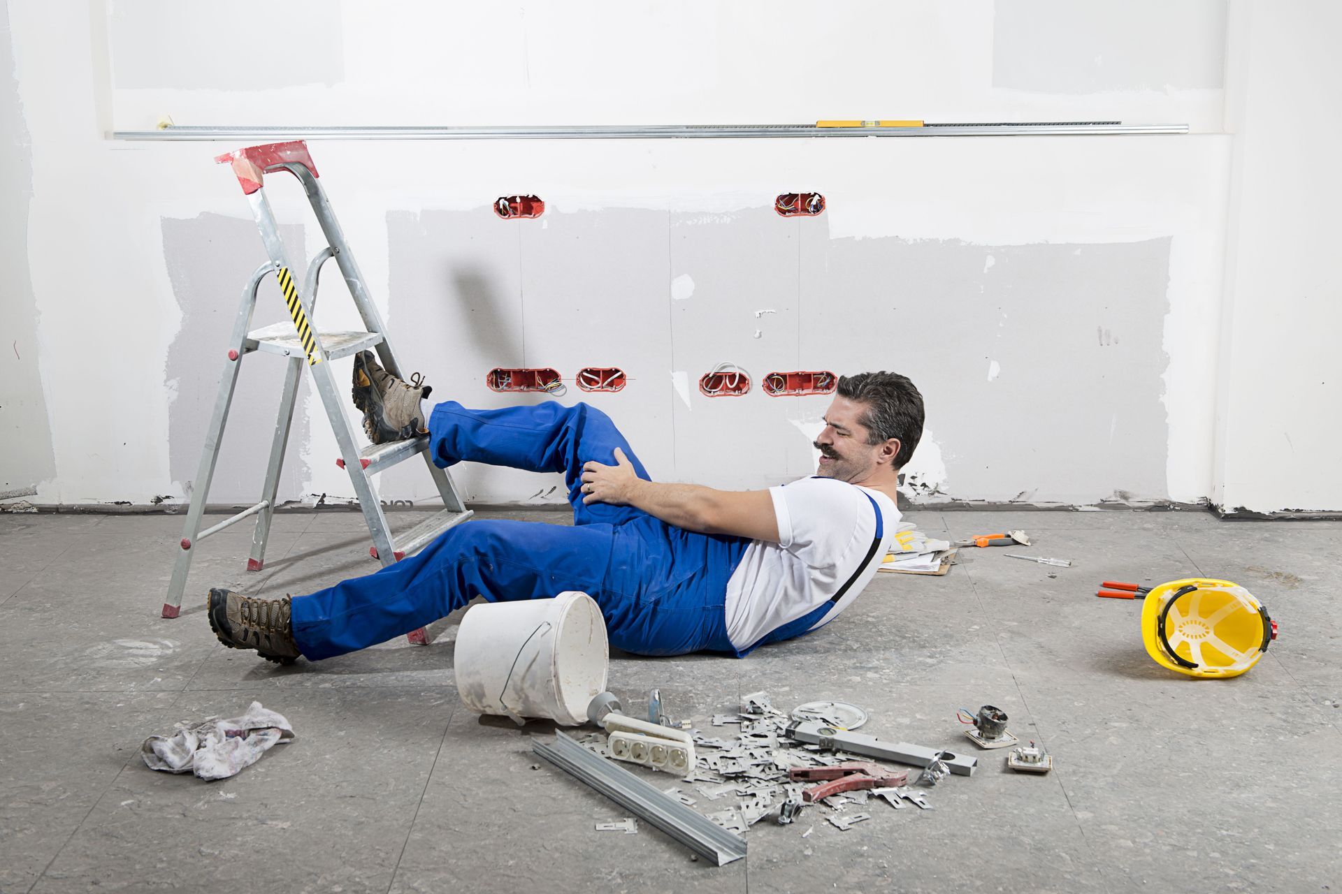An injured worker who fell off a ladder and is lying on the ground, grabbing their leg.