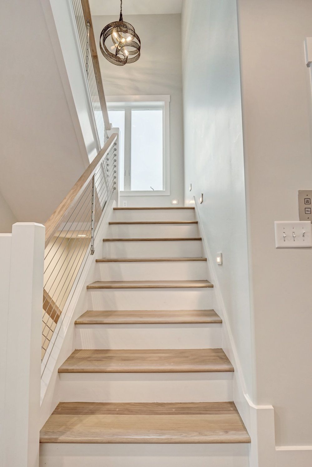 A white staircase with wooden steps leading up to the second floor of a house.