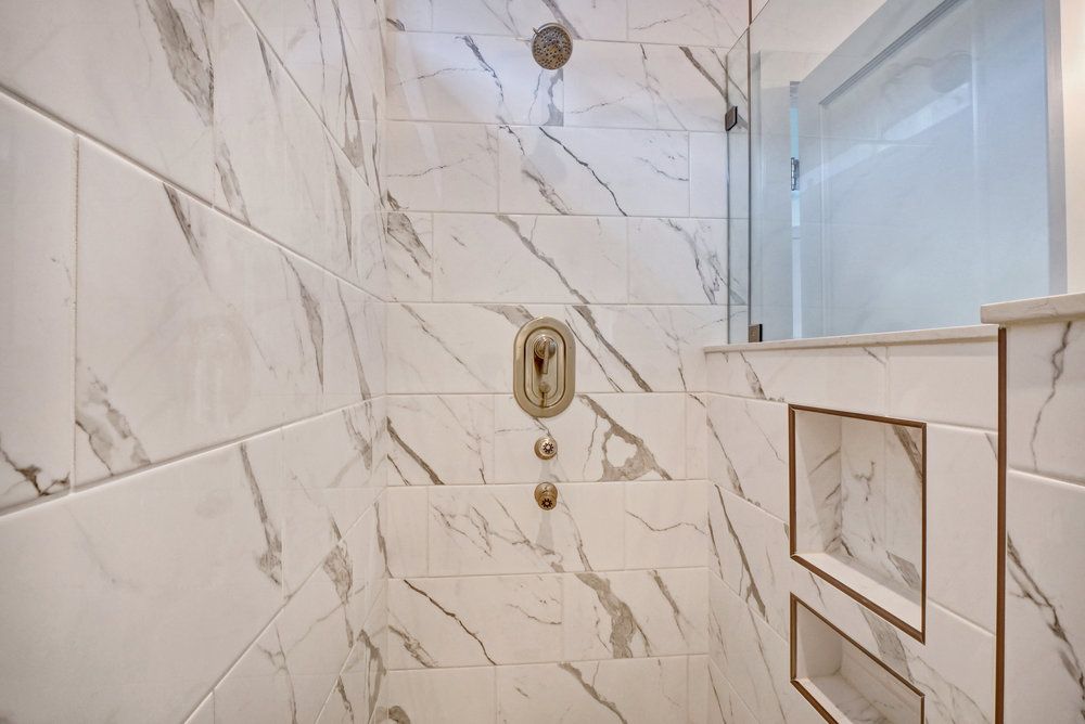 A bathroom with marble tiles and a walk in shower with a glass door.