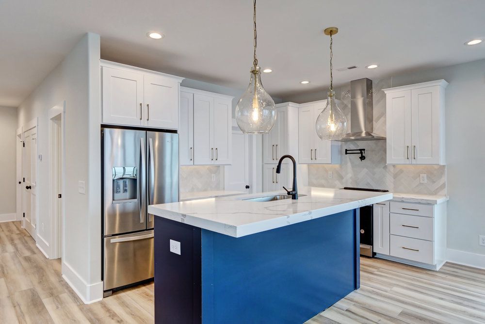 A kitchen with white cabinets , stainless steel appliances , and a blue island.