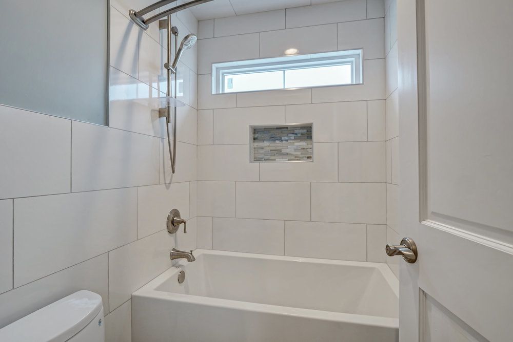 A bathroom with a tub , toilet , shower and window.