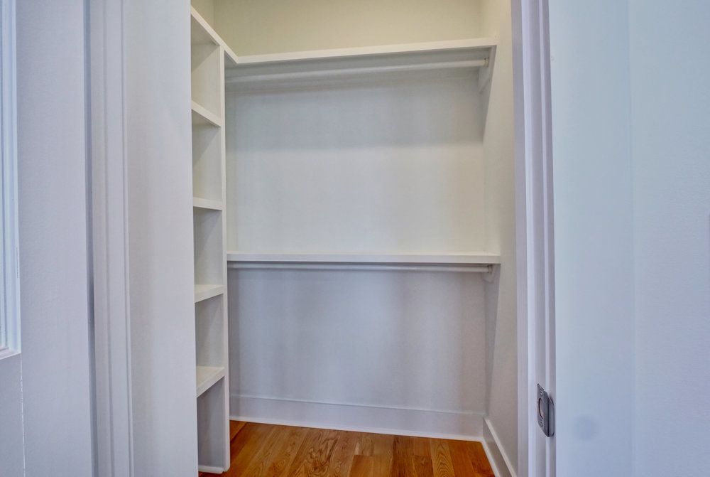 A walk in closet with hardwood floors and white shelves.