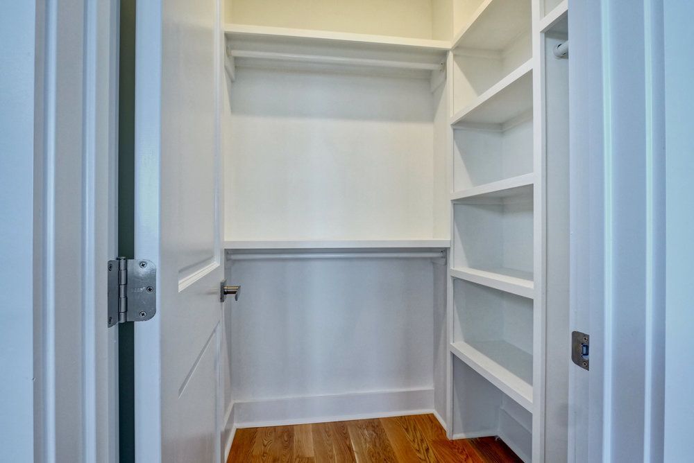 A walk in closet with white shelves and a wooden floor.
