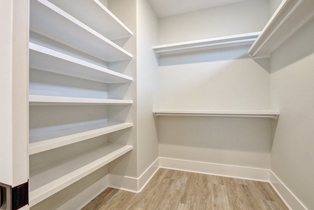 A walk in closet with wooden floors and white shelves.