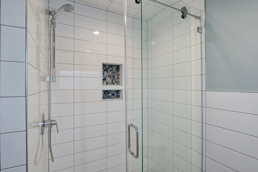 A bathroom with white tiles and a glass shower door.
