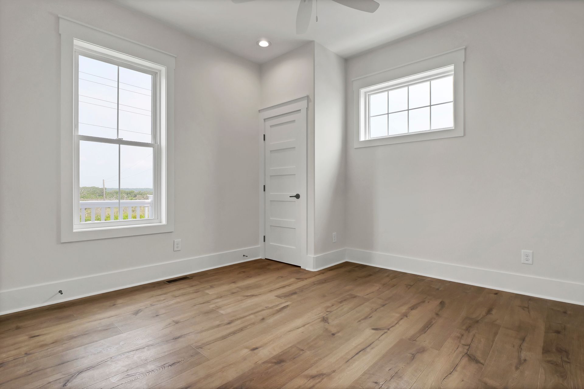 An empty bedroom with hardwood floors , two windows and a ceiling fan.