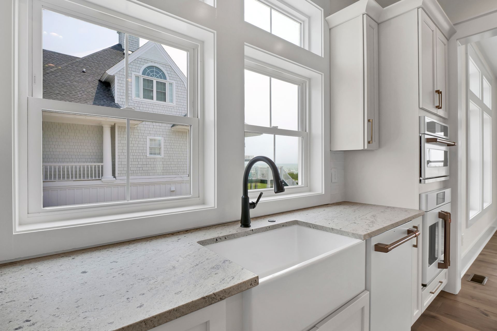 A kitchen with a sink and a window with a view of a house.