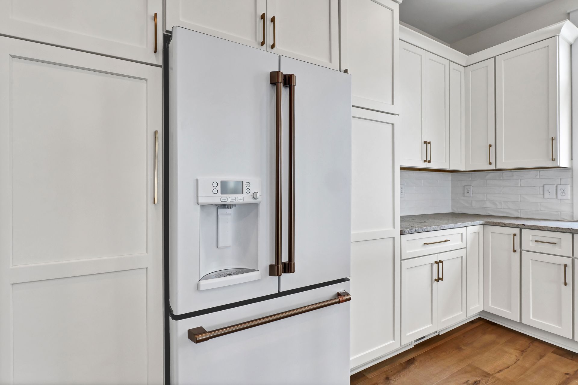 A kitchen with white cabinets and a white refrigerator with a water dispenser.
