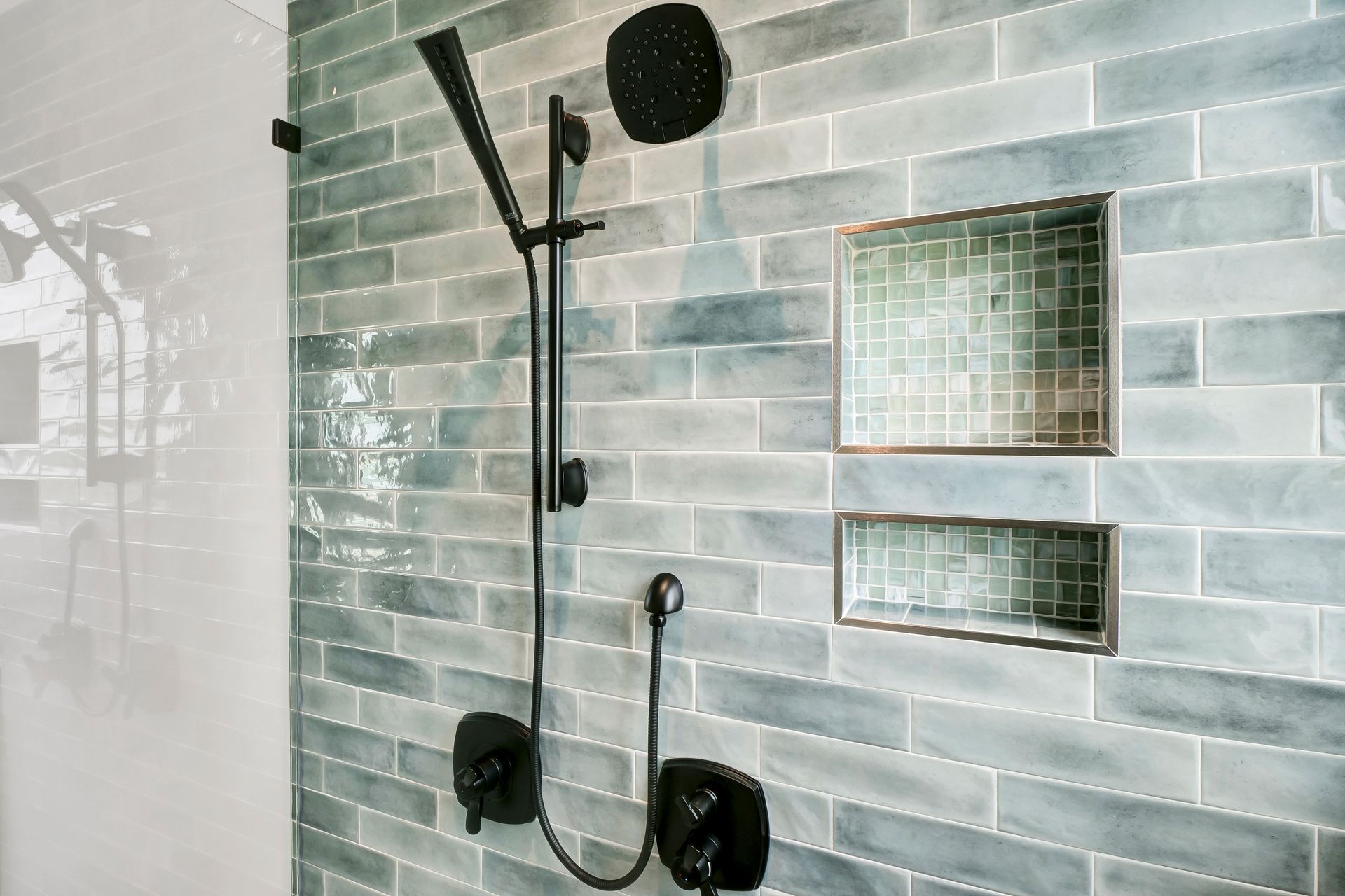 A shower with blue tiles and a black shower head.