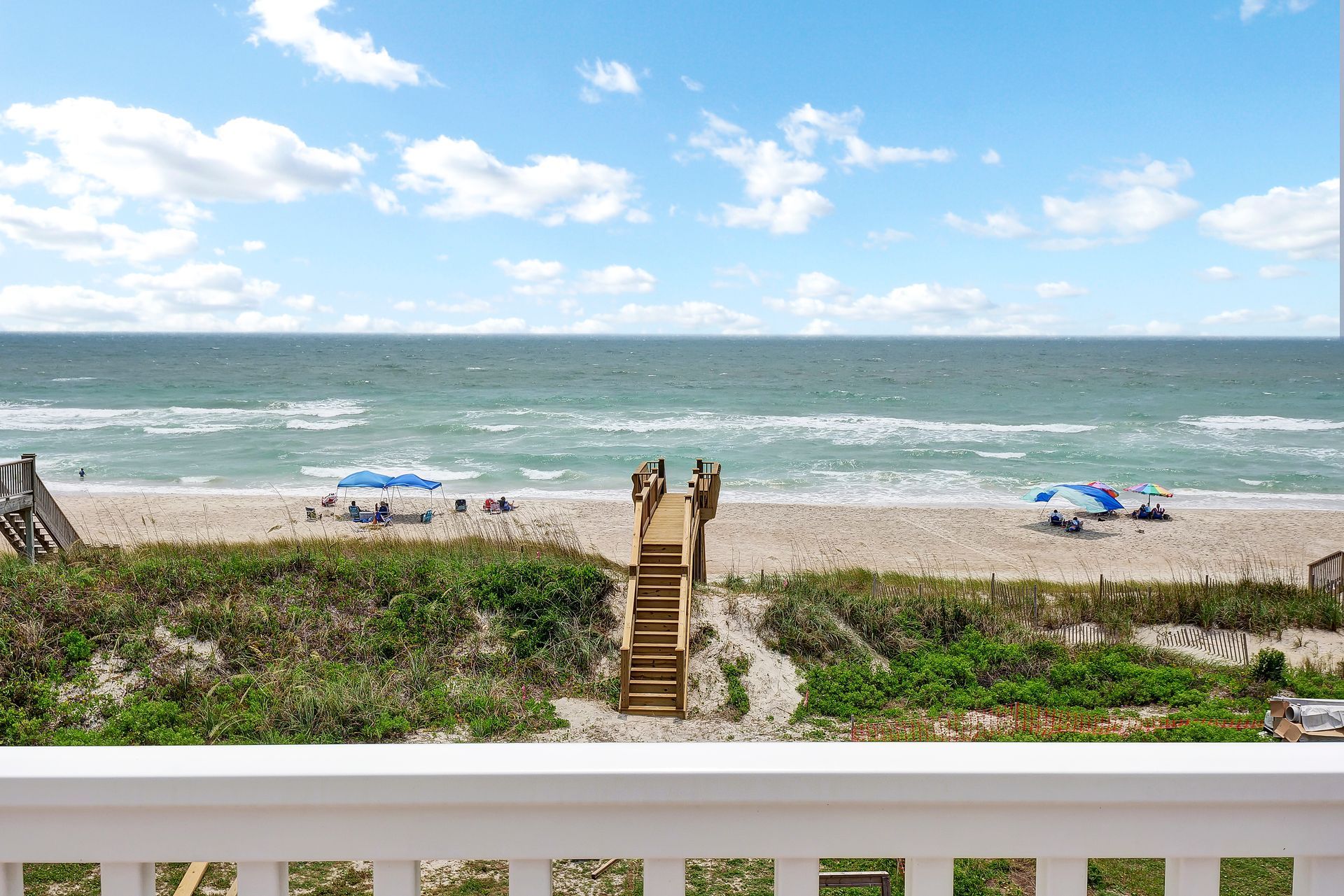 A view of the ocean from a balcony with stairs leading to the beach.