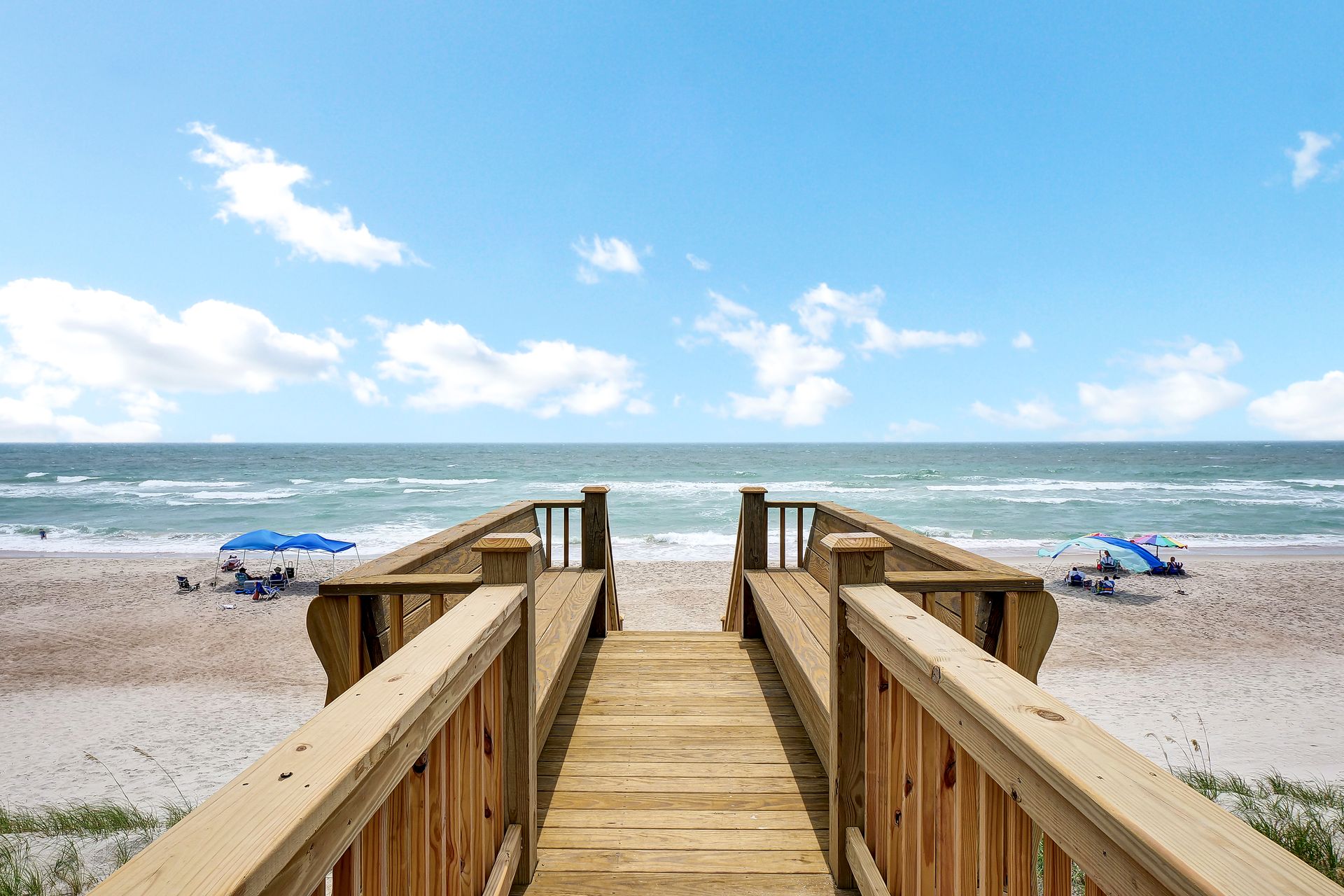 A wooden walkway leading to a beach with umbrellas and chairs.