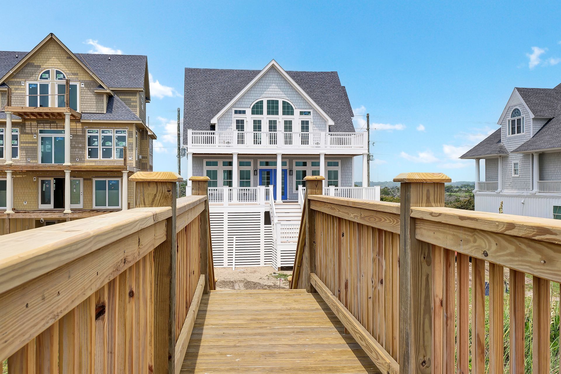 A wooden walkway leading to a large white house.