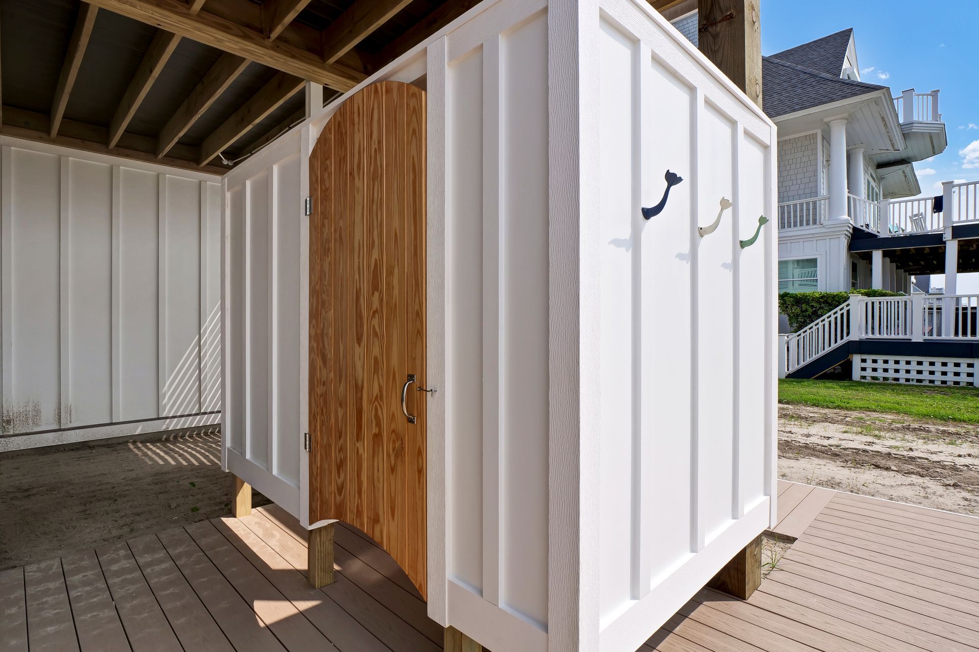 A white shed with wooden doors is sitting on a wooden deck next to a house.