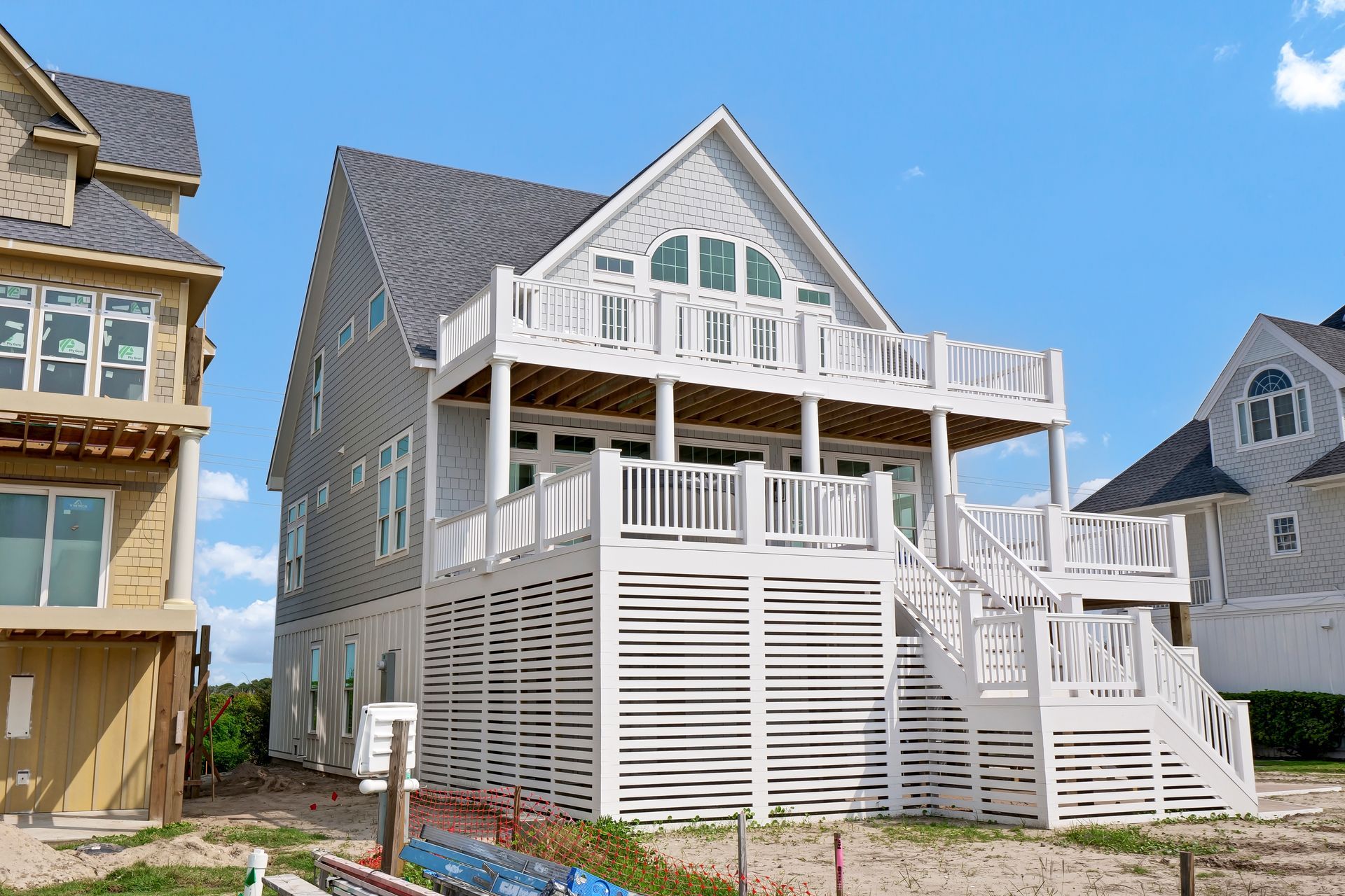 A large white house with a large deck is sitting on top of a sandy beach.