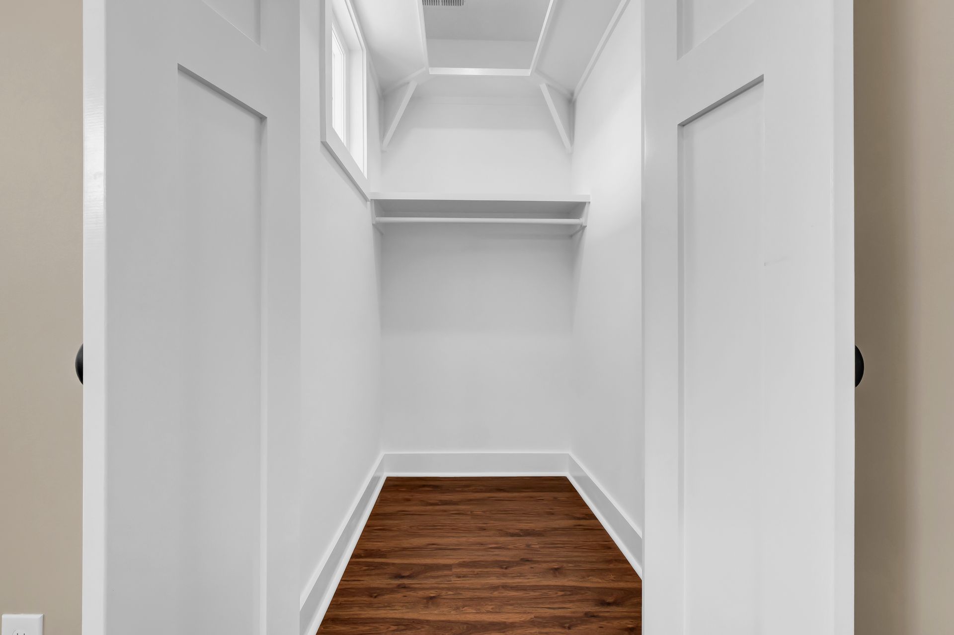 An empty walk in closet with hardwood floors and white walls.