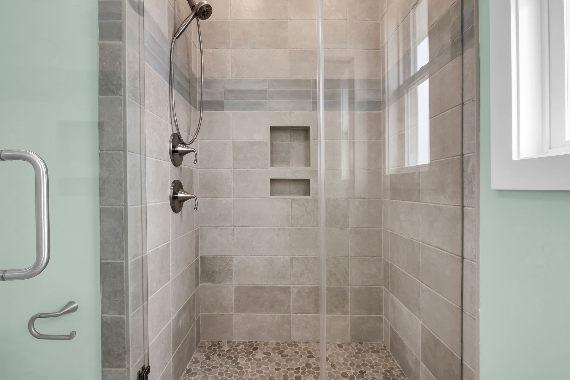 A bathroom with a walk in shower with a glass door and a window.