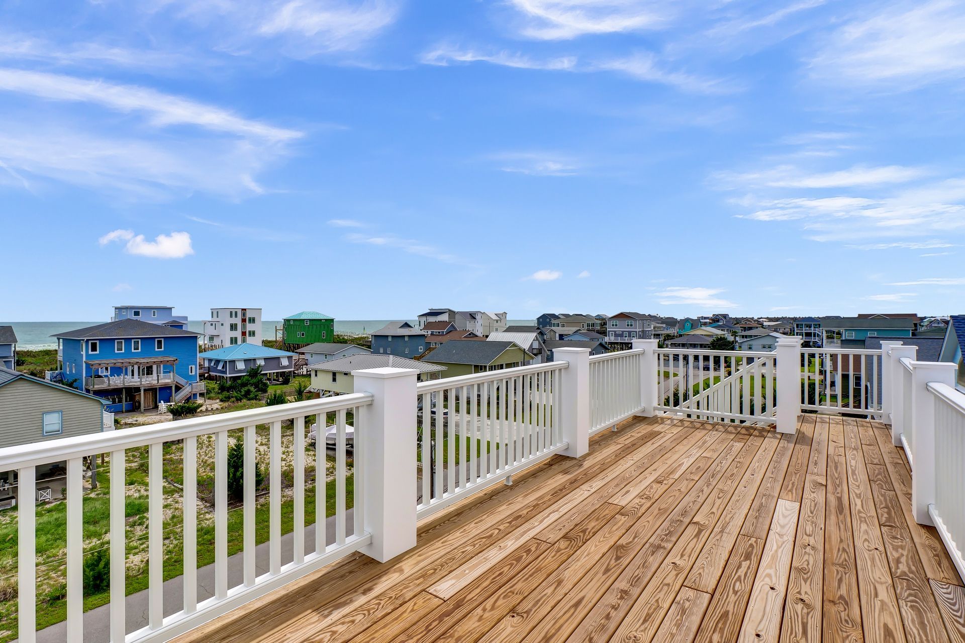 A large wooden deck with a white railing and a view of the ocean.