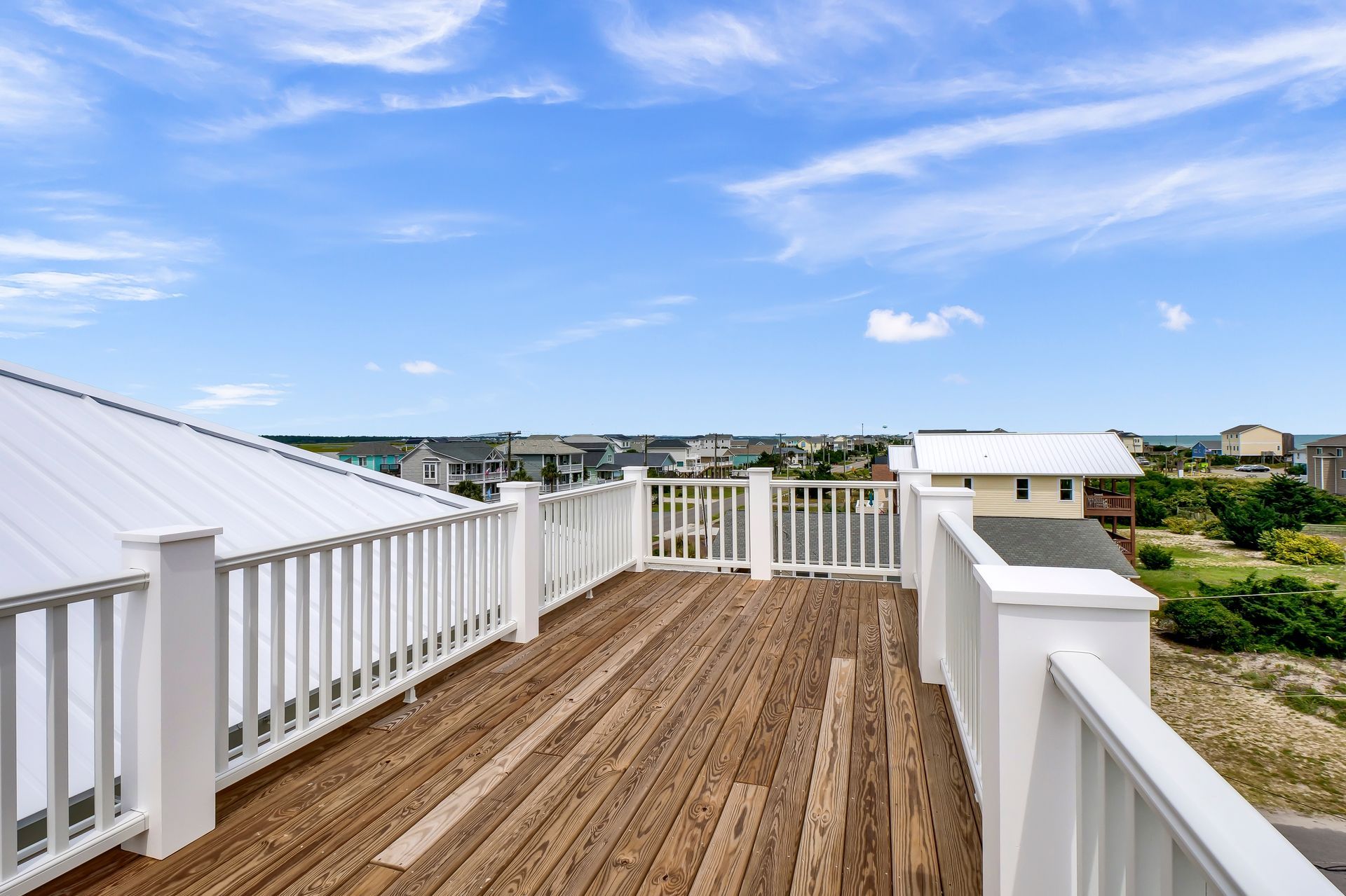 A large wooden deck with a white railing and a view of the ocean.