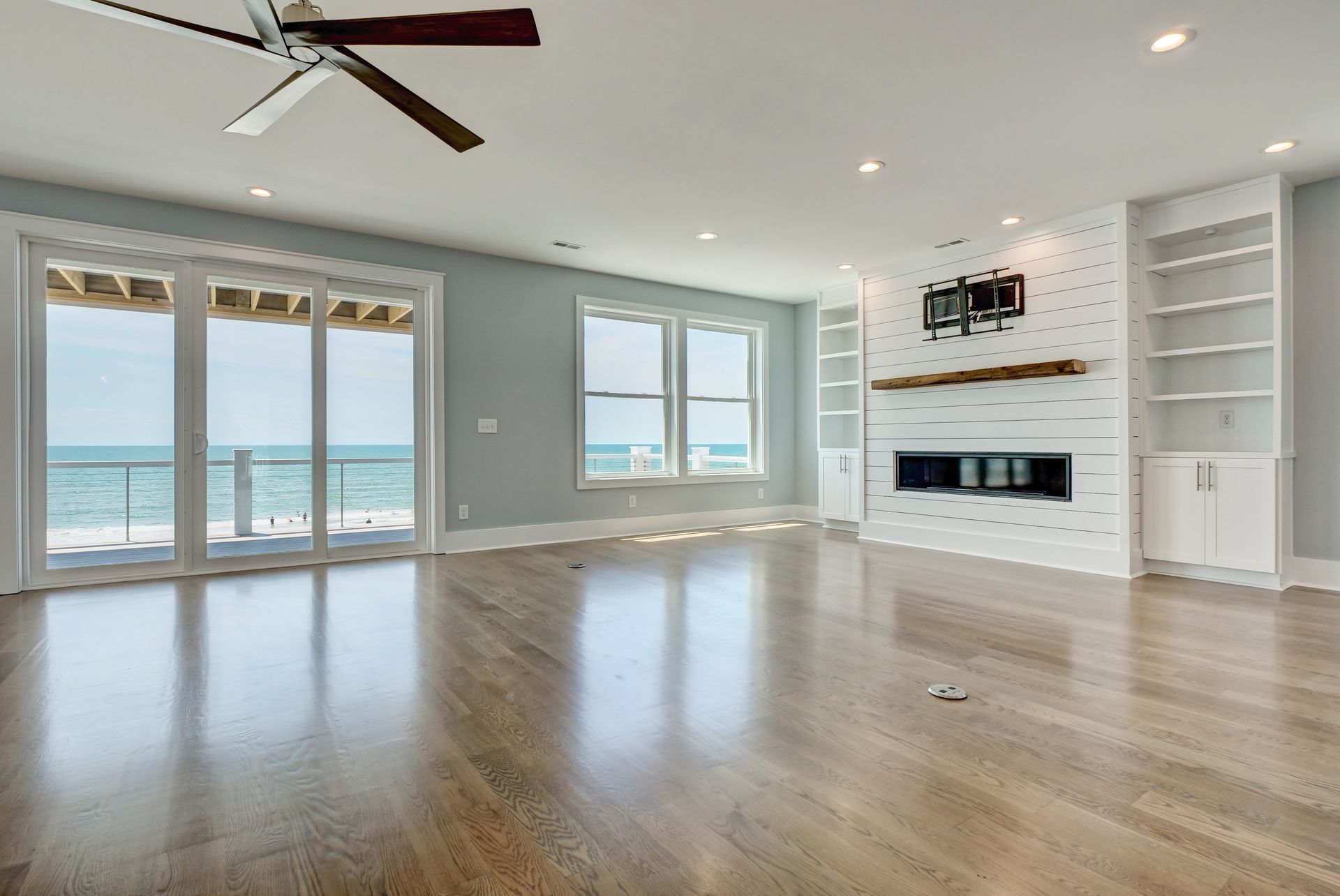 An empty living room with hardwood floors , a fireplace and a ceiling fan.