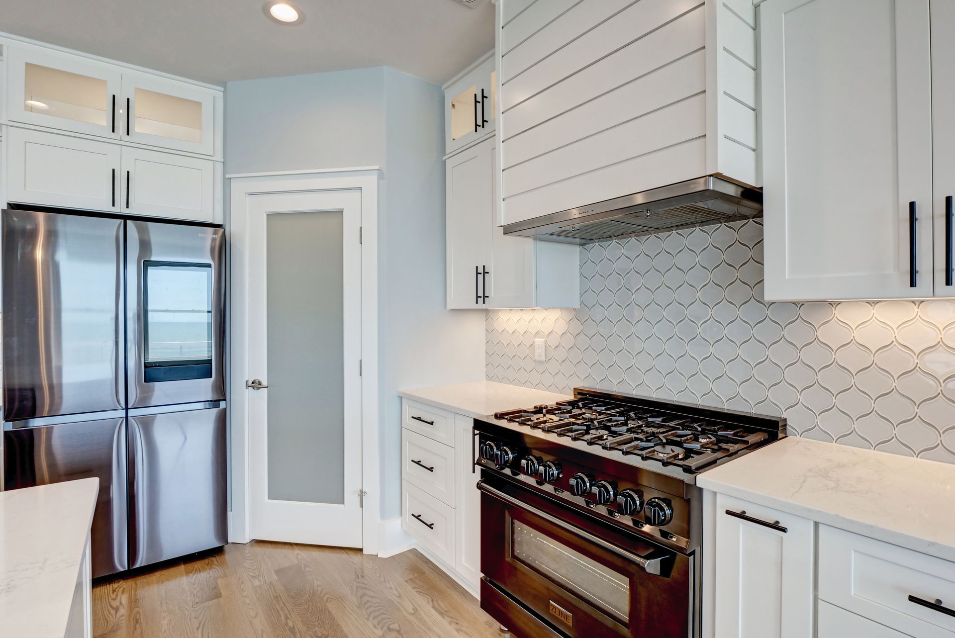 A kitchen with white cabinets , stainless steel appliances , a stove and a refrigerator.