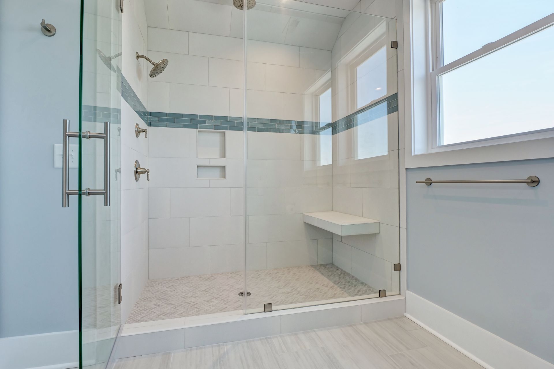 A bathroom with a walk in shower with a glass door and a bench.