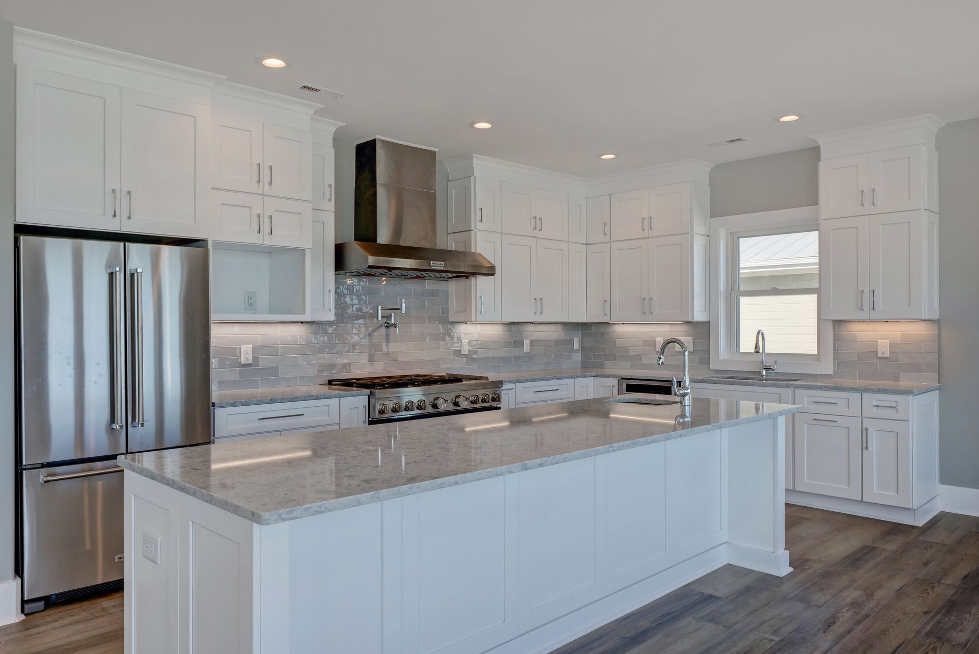 A kitchen with white cabinets , granite counter tops , stainless steel appliances and a large island.