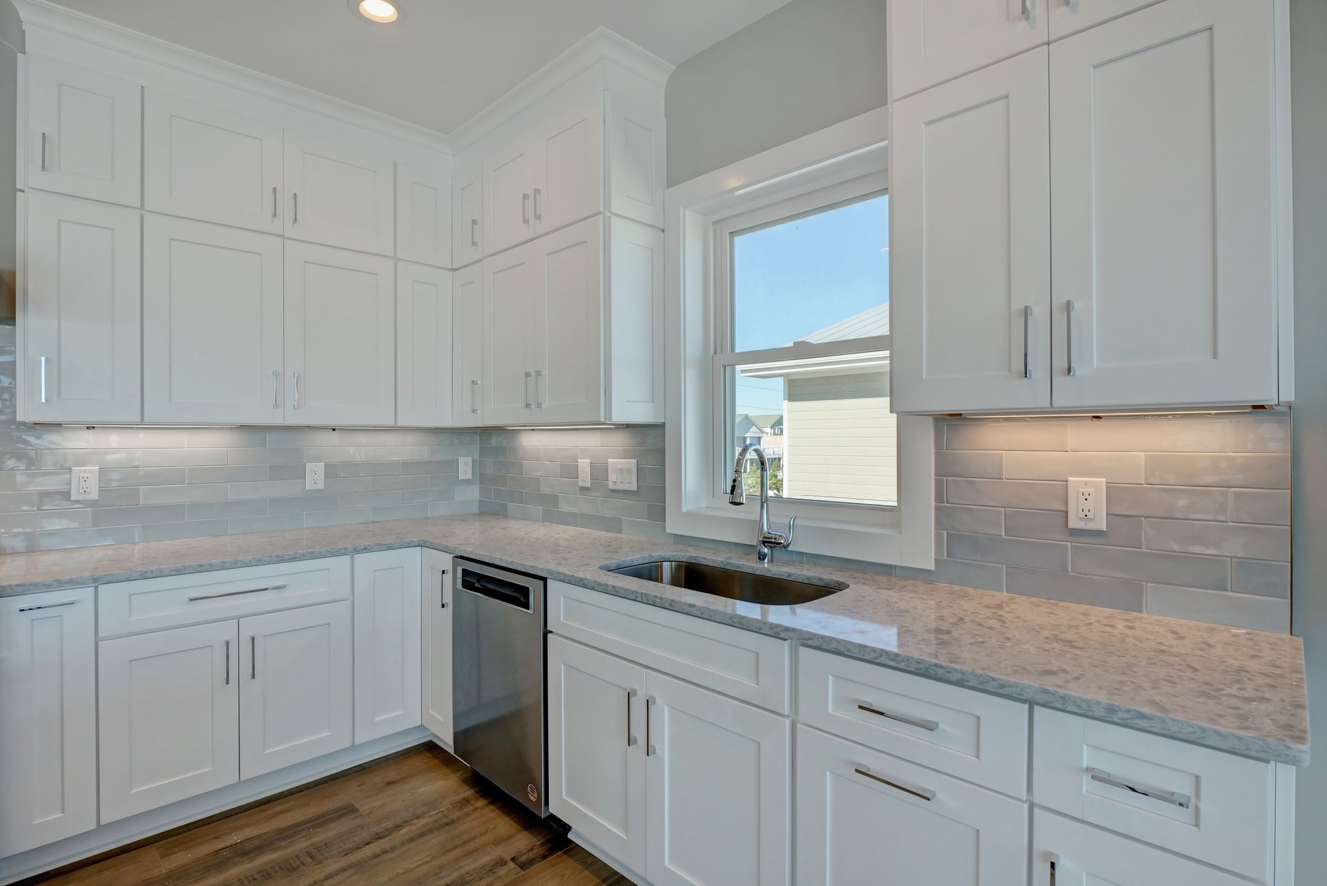 A kitchen with white cabinets , granite counter tops , stainless steel appliances and a window.