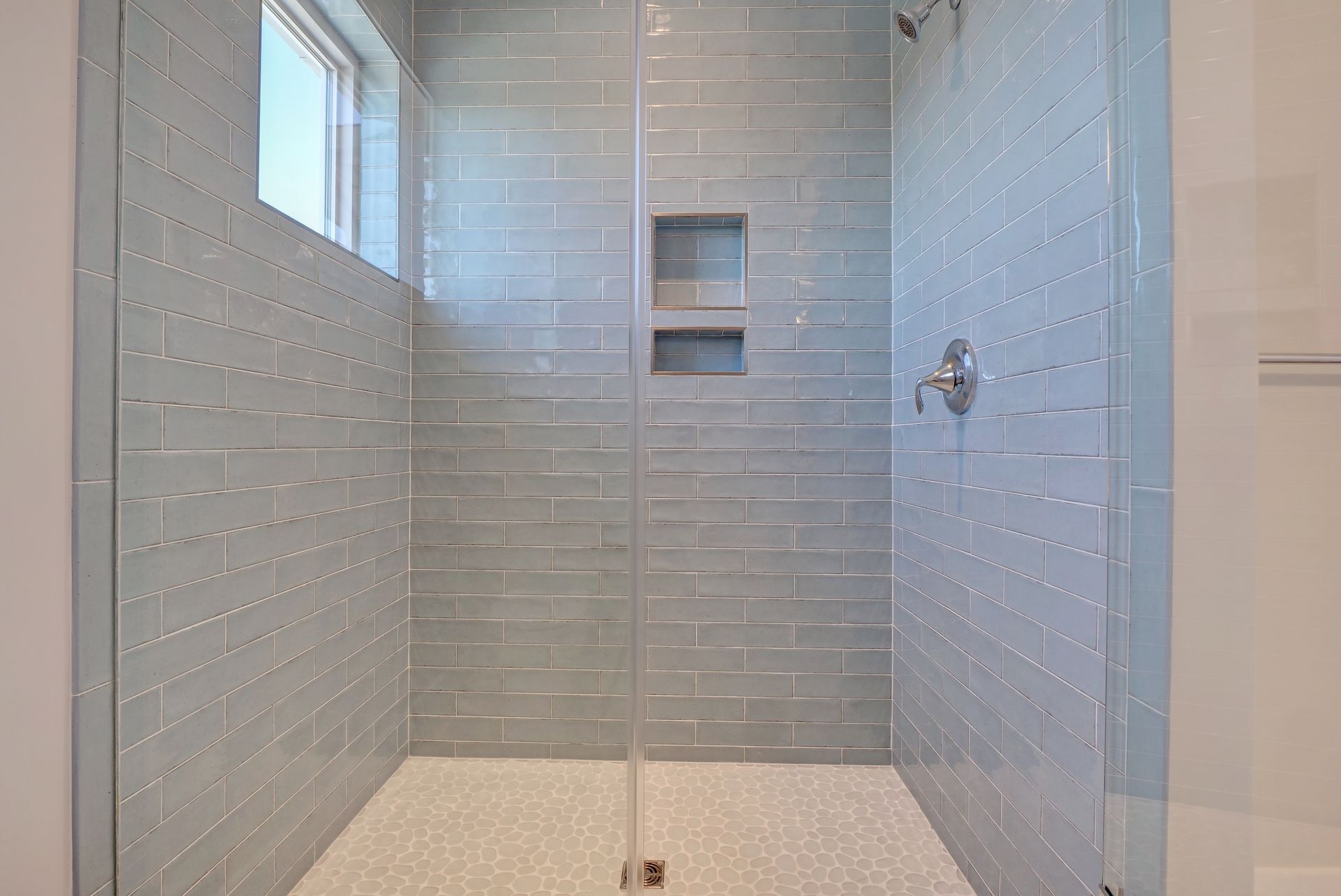A walk in shower with a glass door and a window.