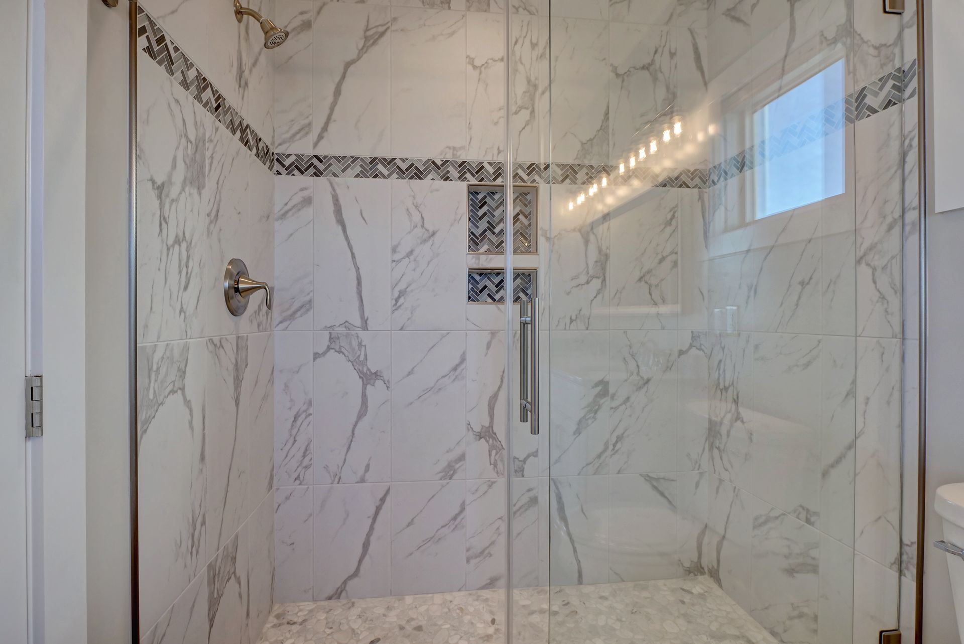 A bathroom with marble tiles and a walk in shower with a glass door.