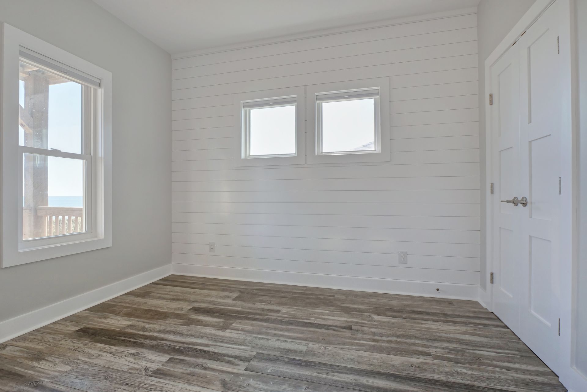 An empty room with a wooden floor and two windows.
