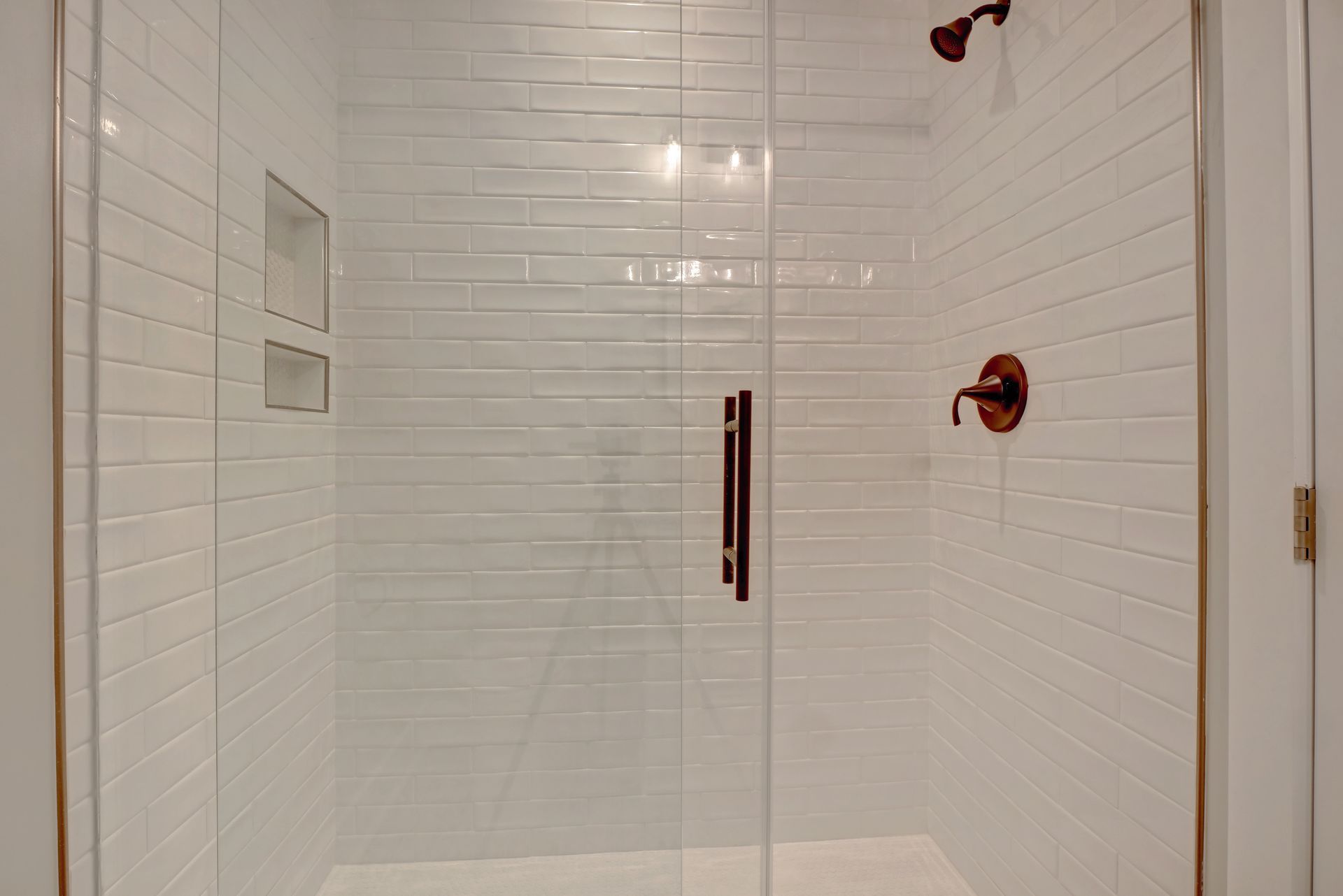 A bathroom with white tiles and a walk in shower with a glass door.