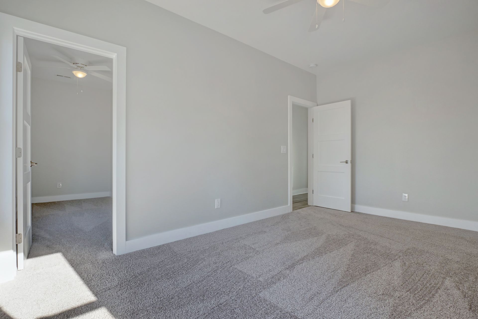 An empty bedroom with a ceiling fan and a gray carpet.