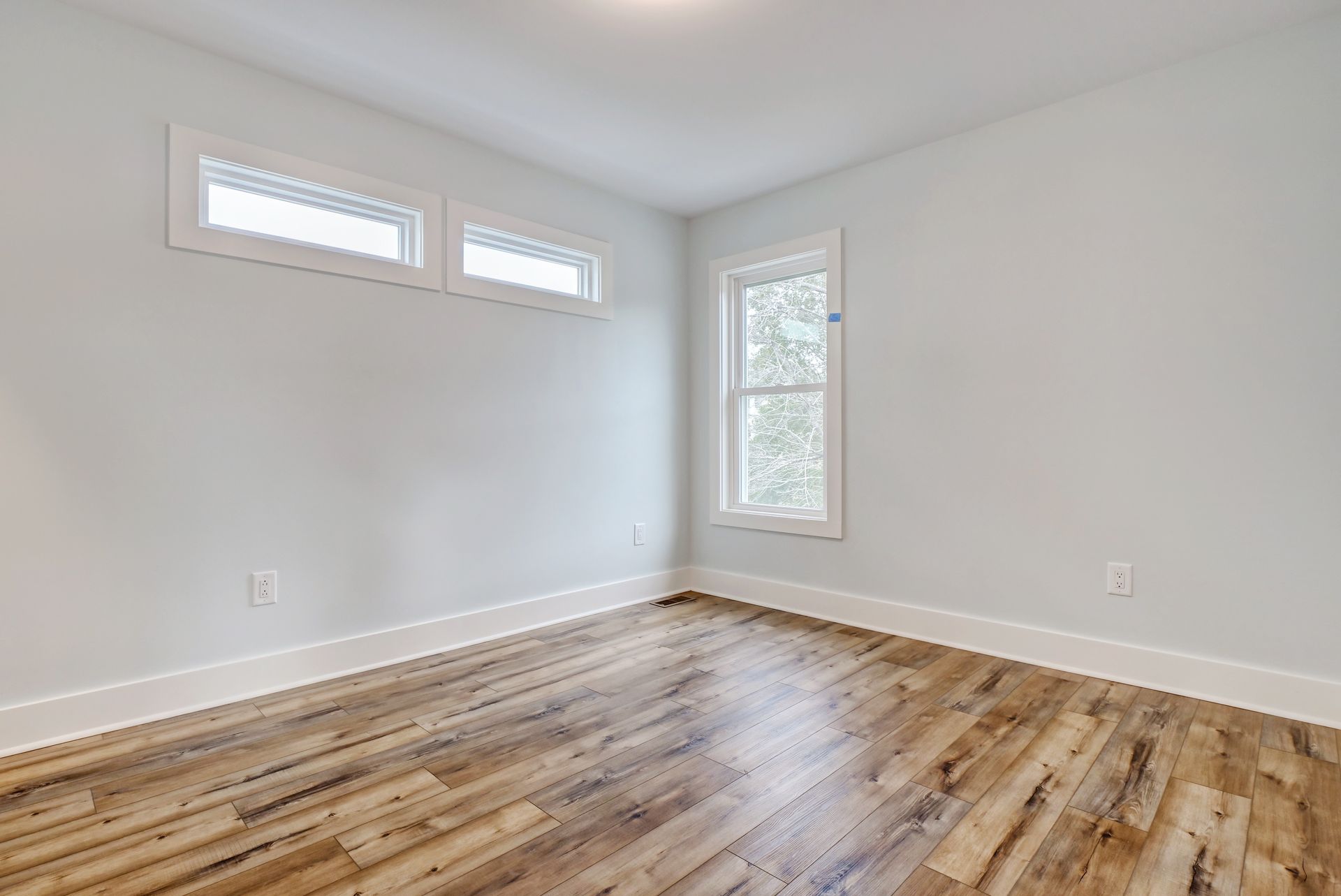 An empty room with hardwood floors and two windows.