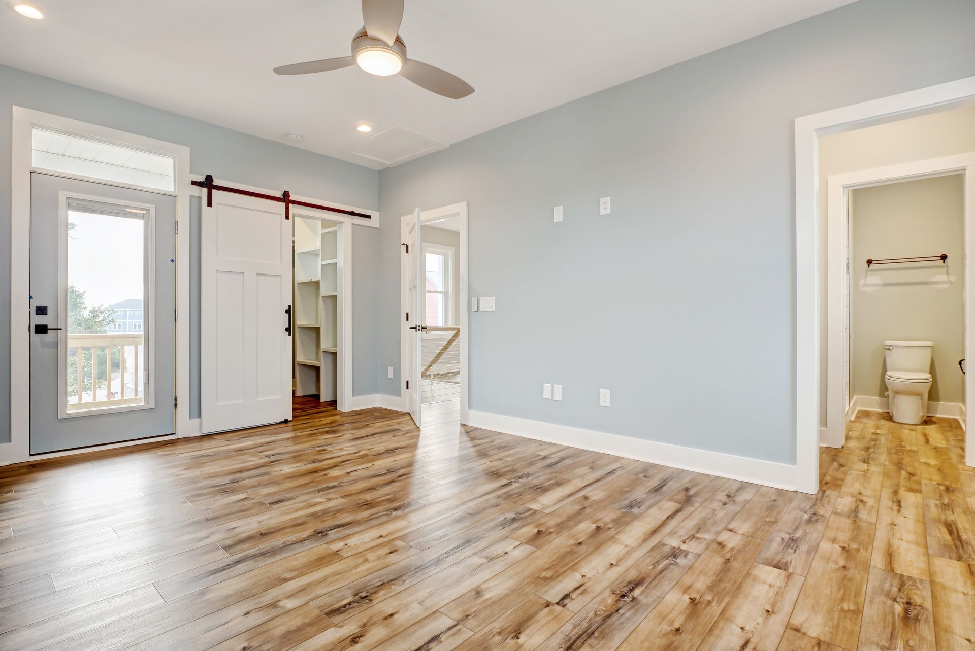 A large empty room with hardwood floors and a ceiling fan.