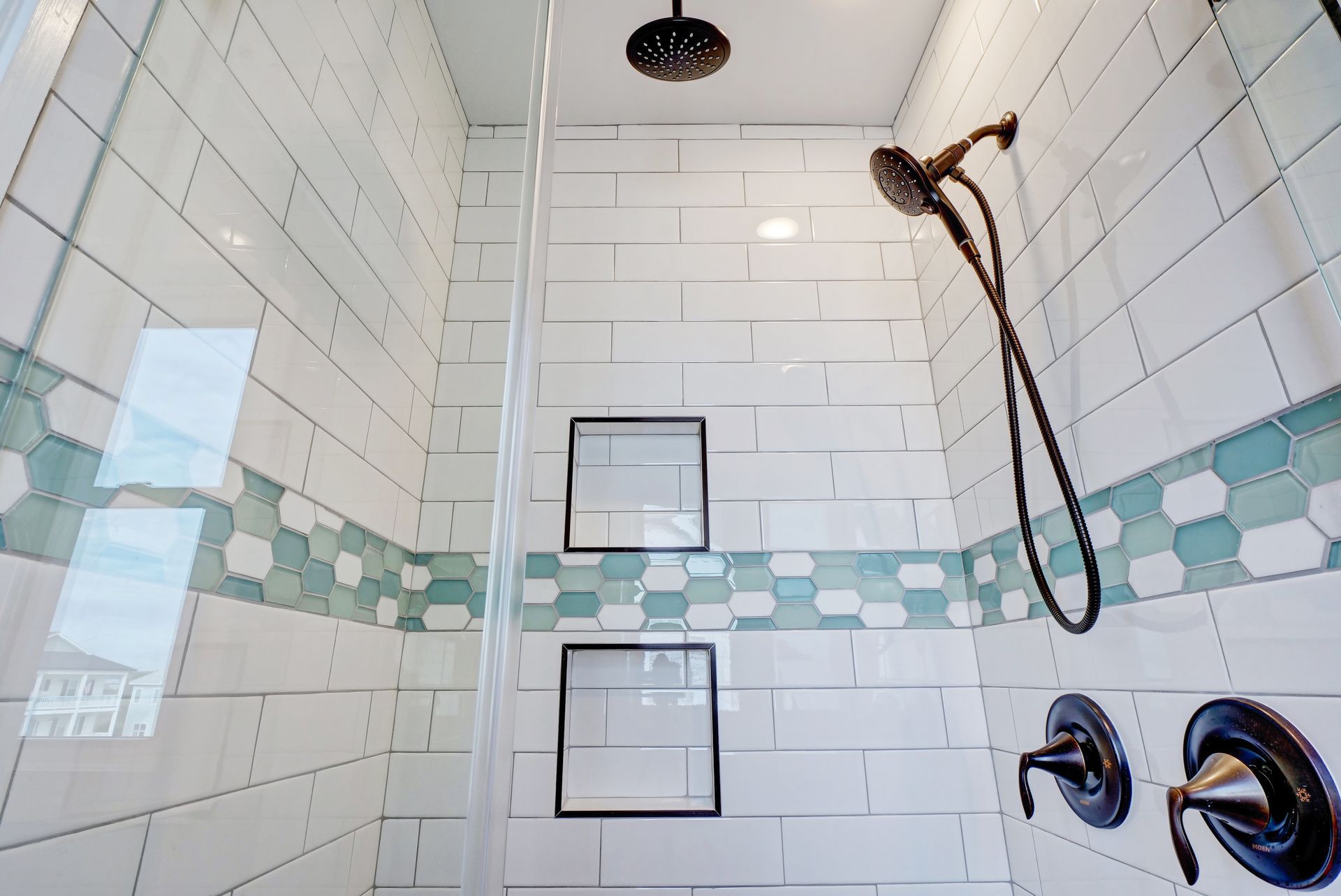 A shower with white tiles and a black shower head.