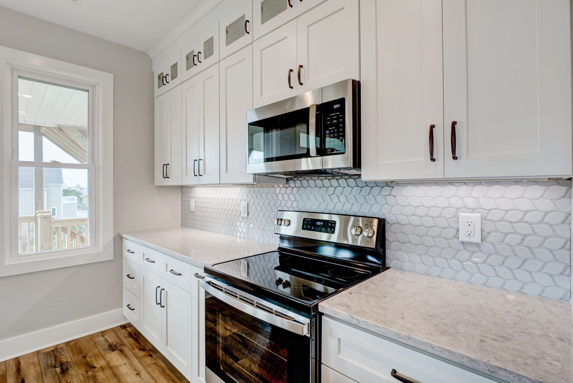 A kitchen with white cabinets , a stove , a microwave , and a window.
