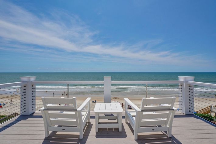 Two white chairs and a table on a balcony overlooking the ocean.