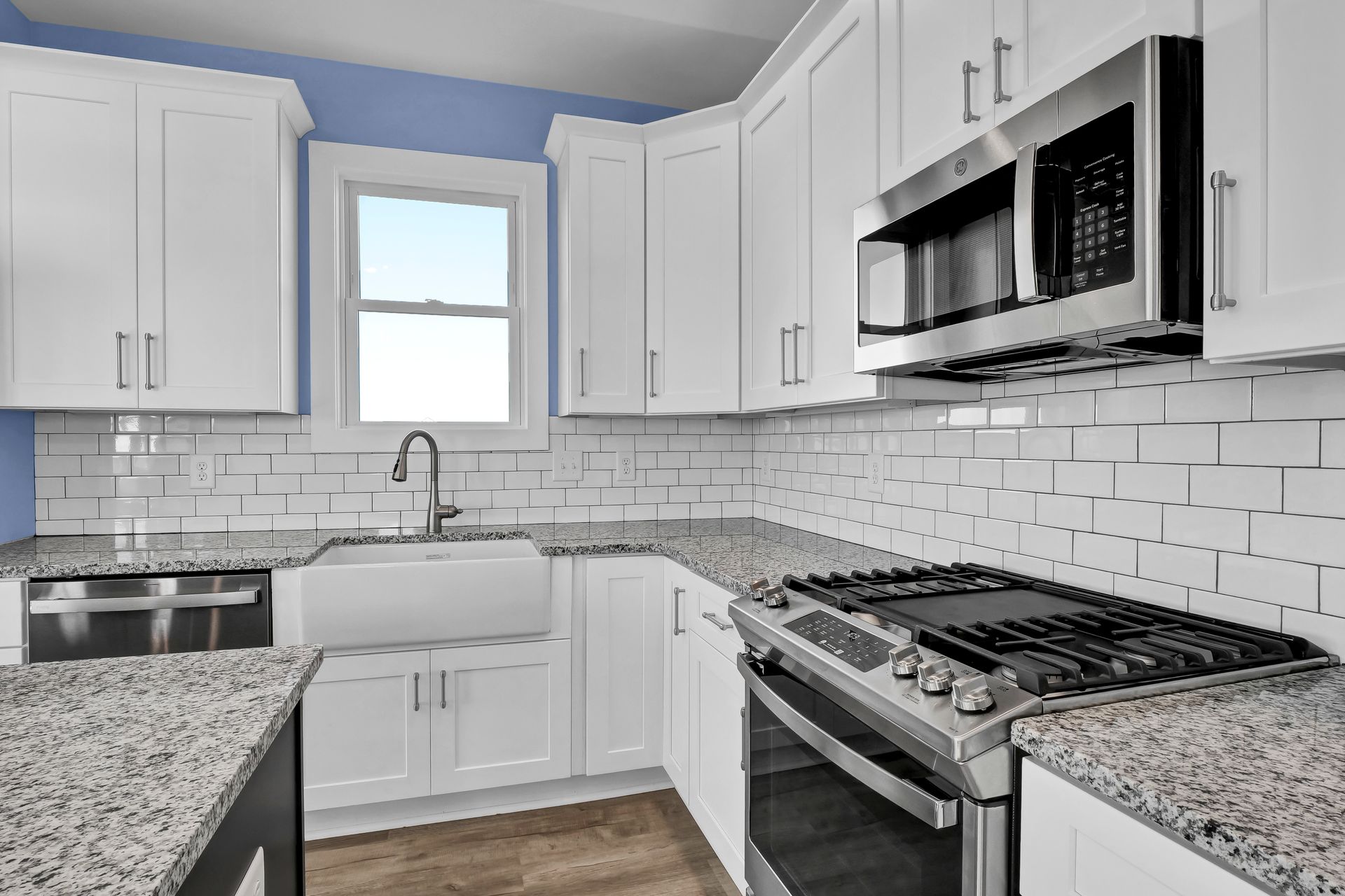 A kitchen with white cabinets , granite counter tops , stainless steel appliances and a stove.