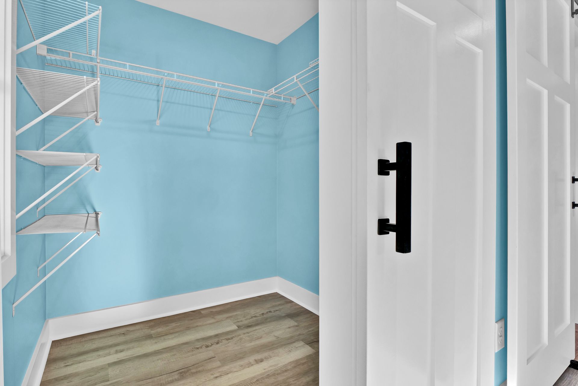 A walk in closet with blue walls and white shelves.