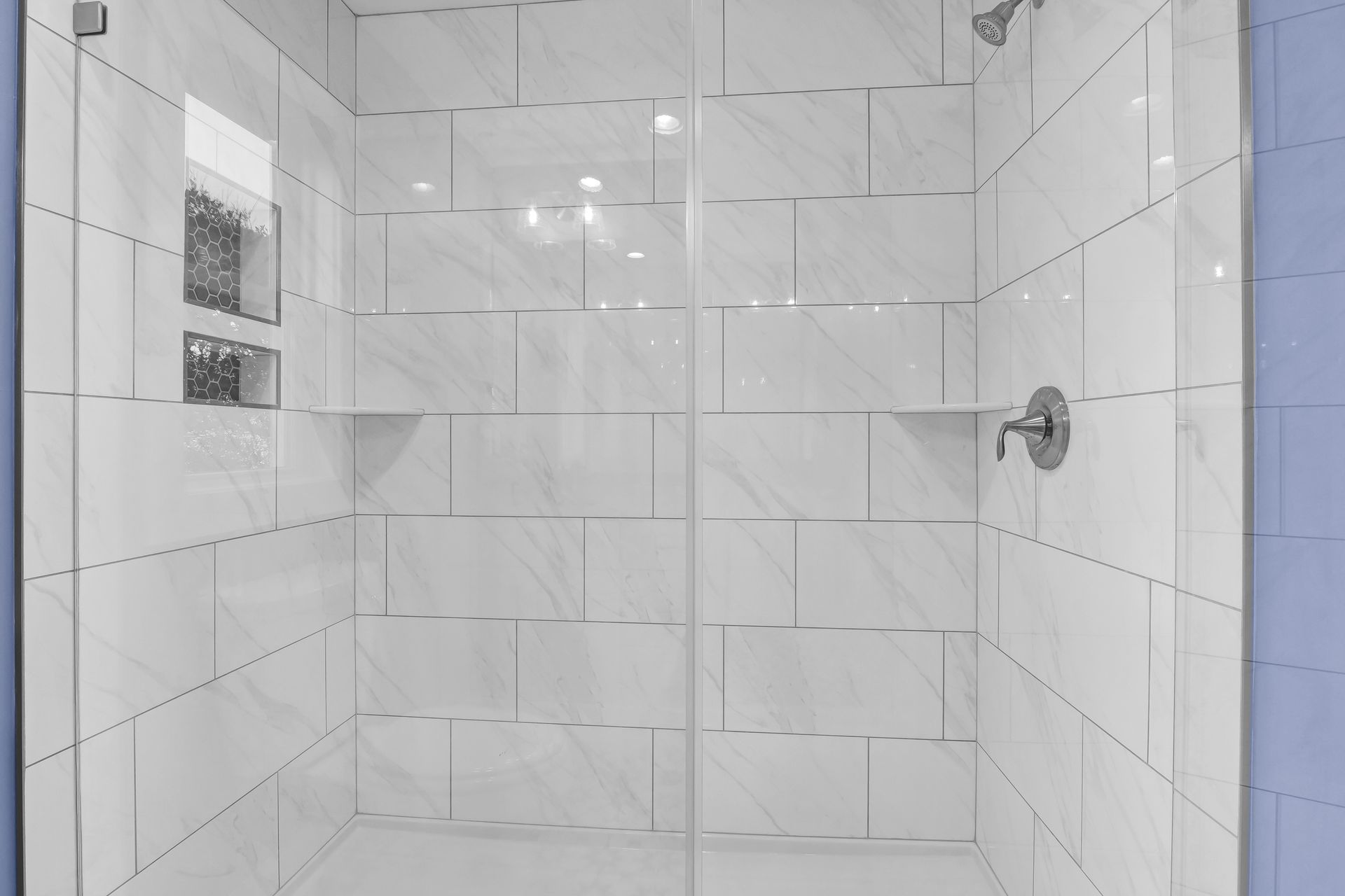 A bathroom with white tiles and a walk in shower with a glass door.