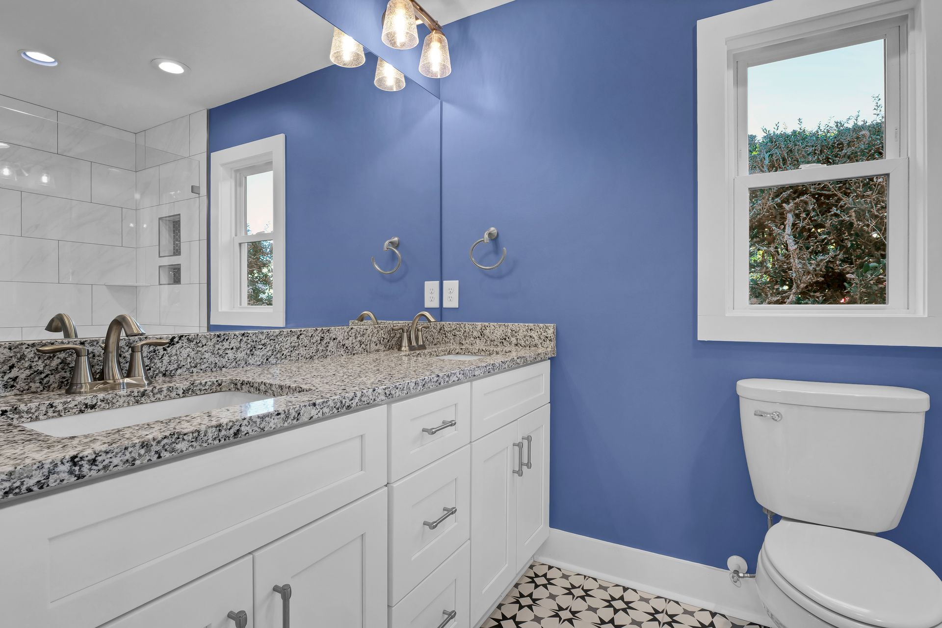 A bathroom with blue walls , white cabinets , a sink and a toilet.