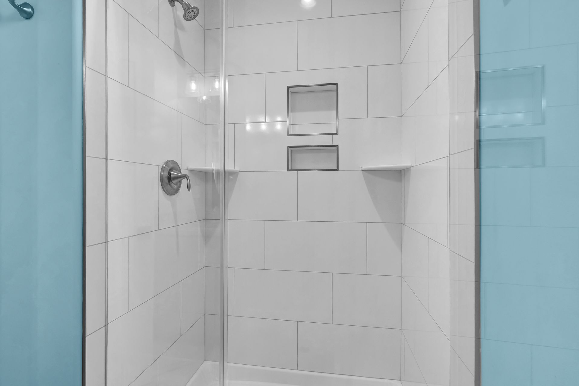 A shower with a glass door and white tiles in a bathroom.